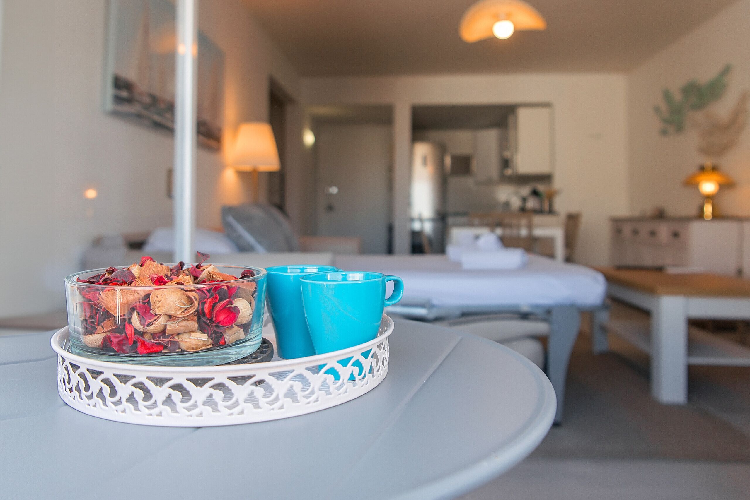 A room with a bed, a table with a decorative tray, and a kitchen area in the background.