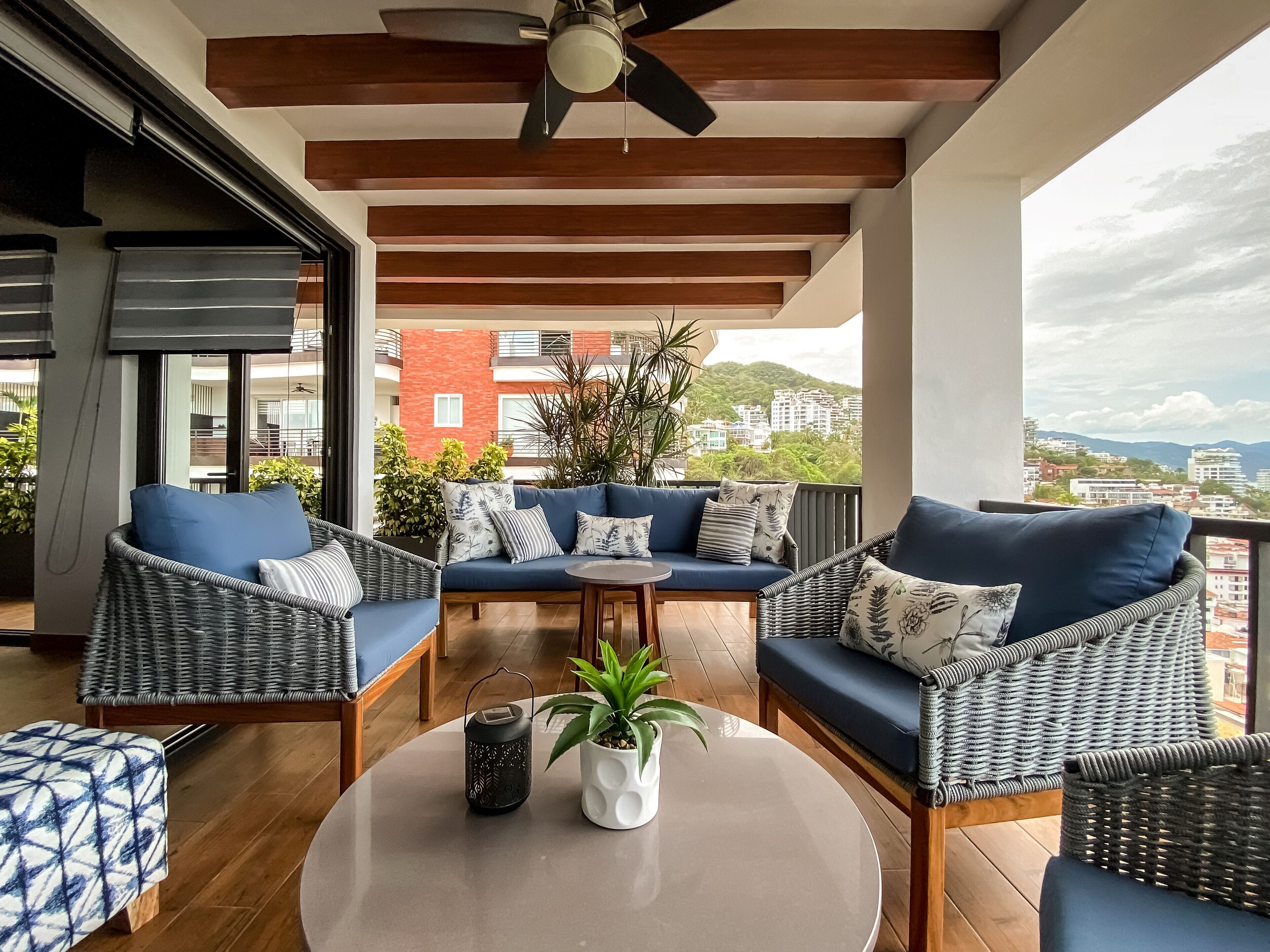 A balcony with wicker furniture, a ceiling fan, and a view of buildings and hills.