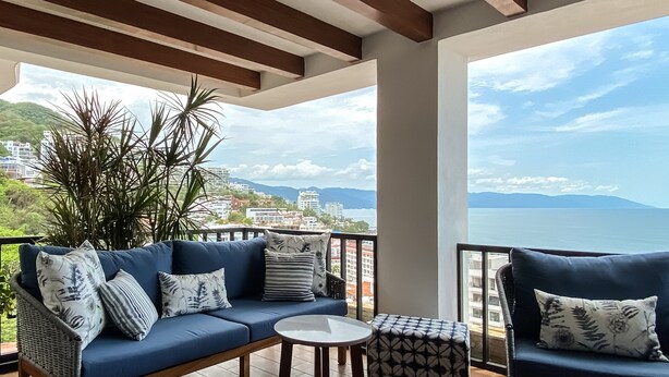 Un balcon avec un canapé bleu, une petite table ronde et une chaise en osier.