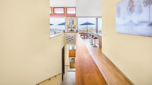 A modern hotel corridor with a wooden floor, large windows, and a view of the cityscape.