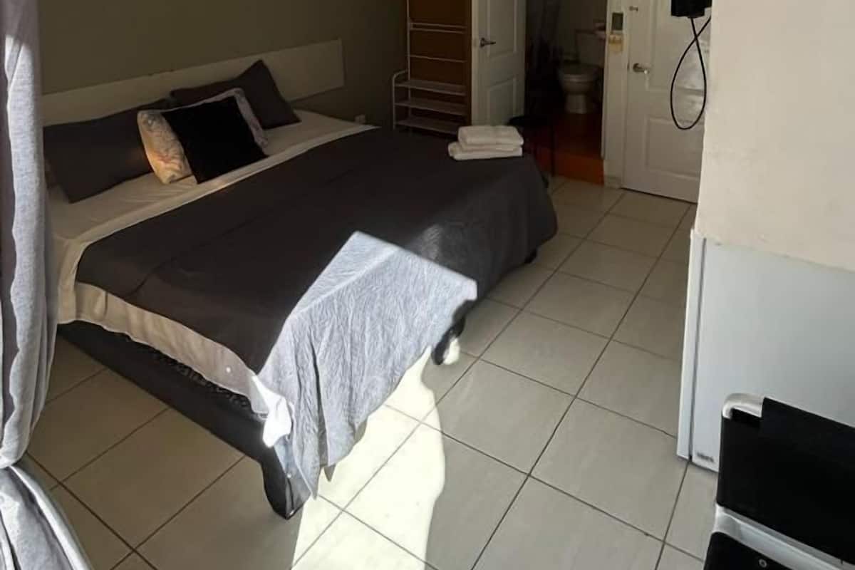 A bedroom with a bed, a ceiling fan, a door leading to a bathroom, and a TV mounted on the wall.