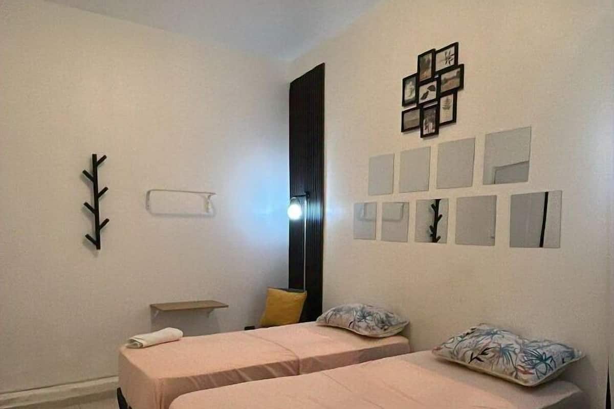 A bedroom with two beds, a wall-mounted light fixture, and a small bedside table with a lamp.