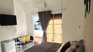 A modern bedroom with a large bed, a ceiling fan, an air conditioning unit, a TV mounted on the wall, and a window with curtains.