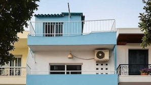 A two-story building with a blue facade, a closed garage door, and a small balcony with a railing.
