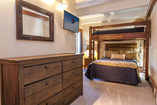A bedroom with a bunk bed, wooden dresser, and a television on the wall.