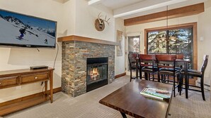 Ein Wohnzimmer mit Kamin aus Stein, einem an der Wand befestigten Fernseher und einem Essbereich mit Holztisch und -stühlen.