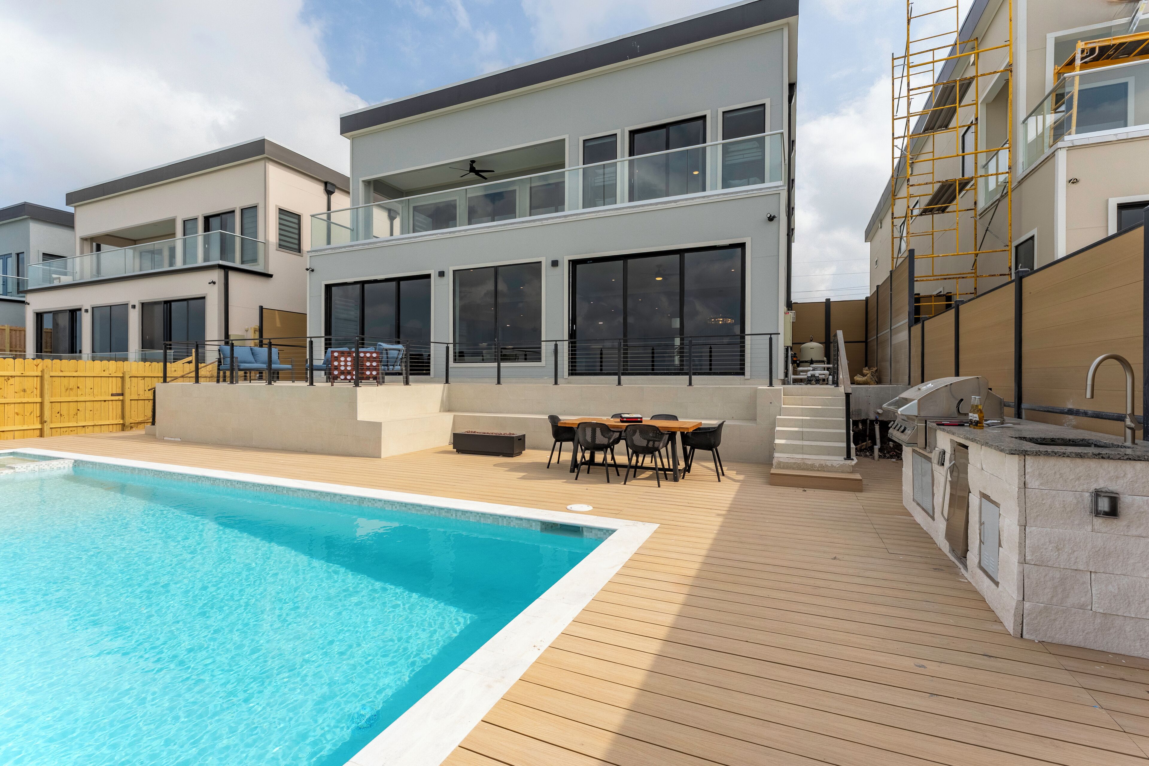 A modern residential building with a swimming pool, outdoor dining area, and a barbecue setup.
