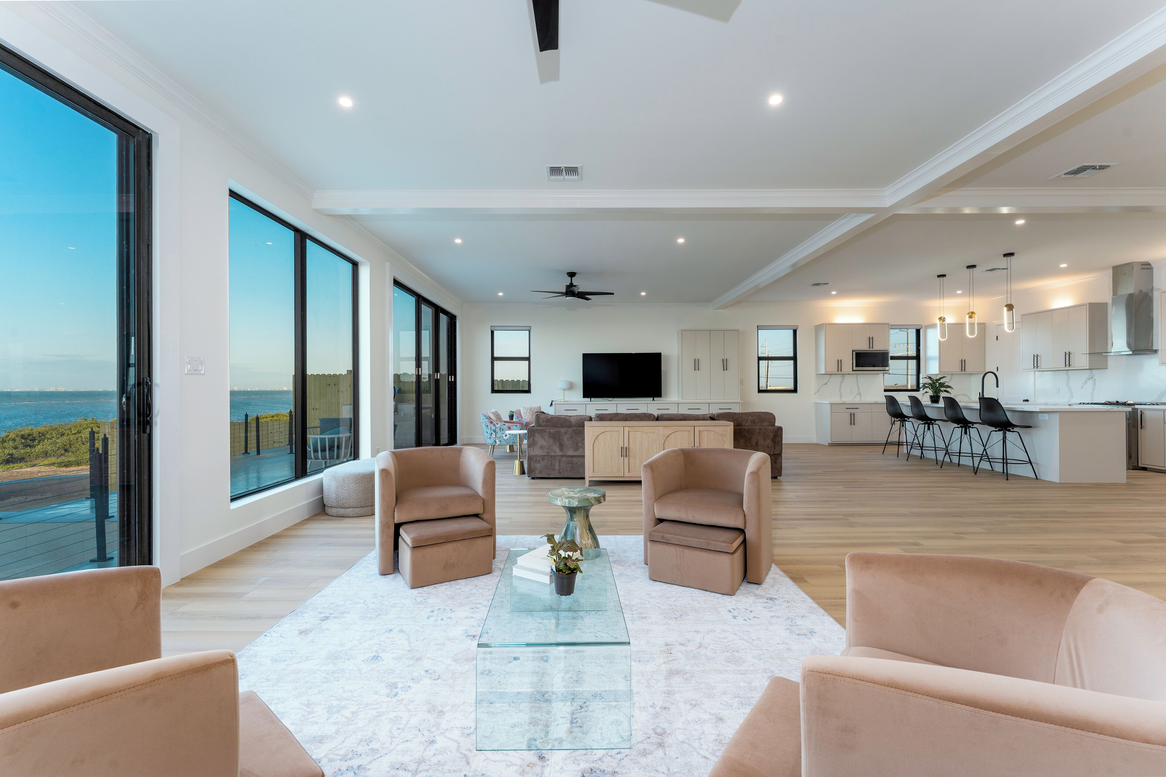A spacious living area with large windows, a flat-screen TV, and a modern kitchen with bar seating.