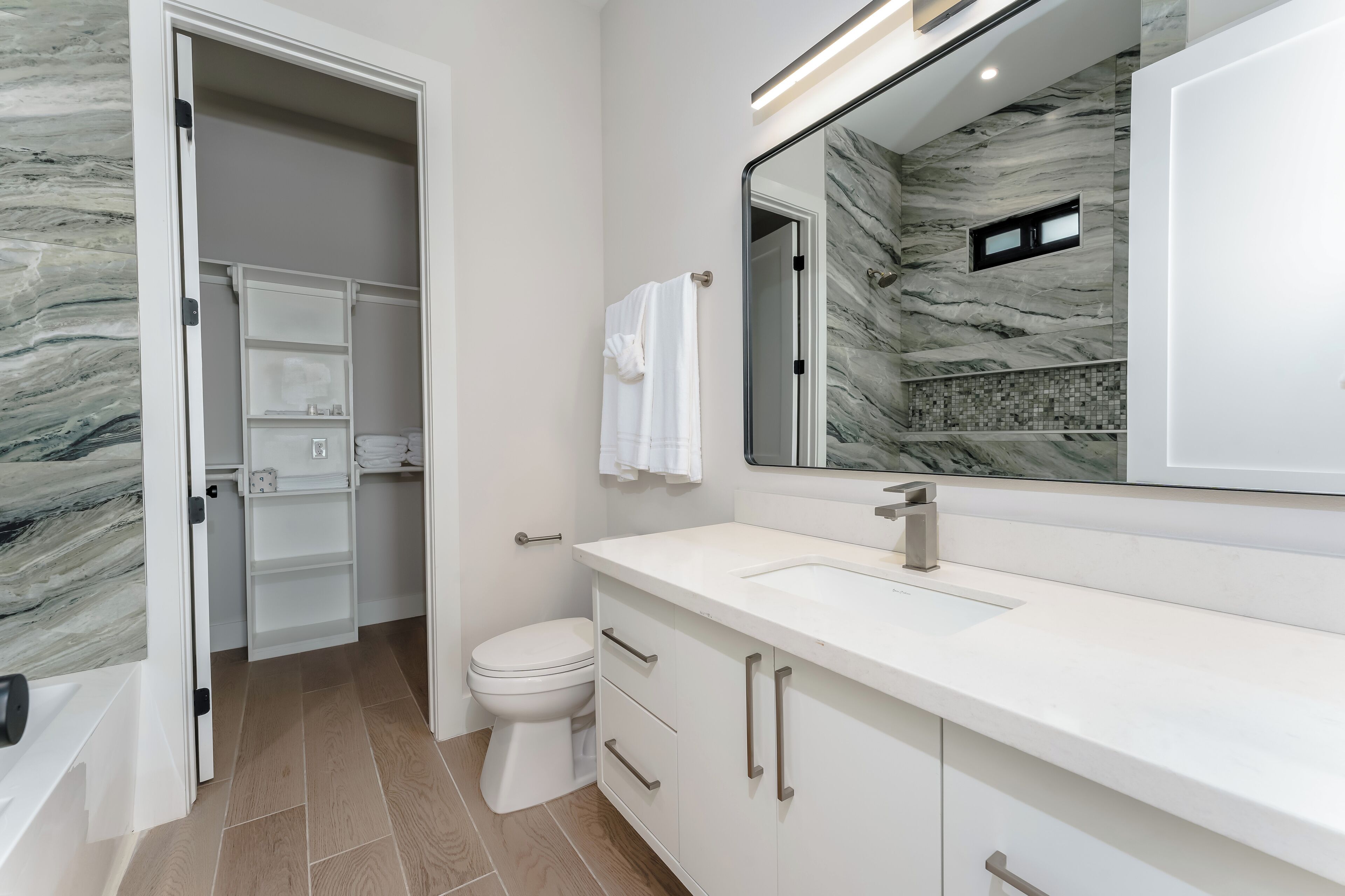 A modern bathroom with a white vanity, a large mirror, and a marble backsplash.
