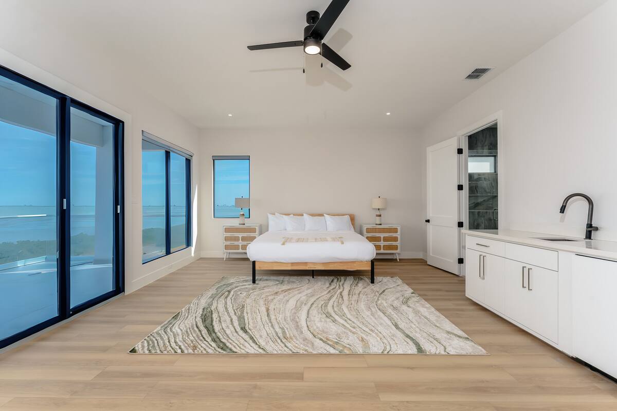 A modern bedroom with a bed, a large window, a ceiling fan, and a view of the outdoors.