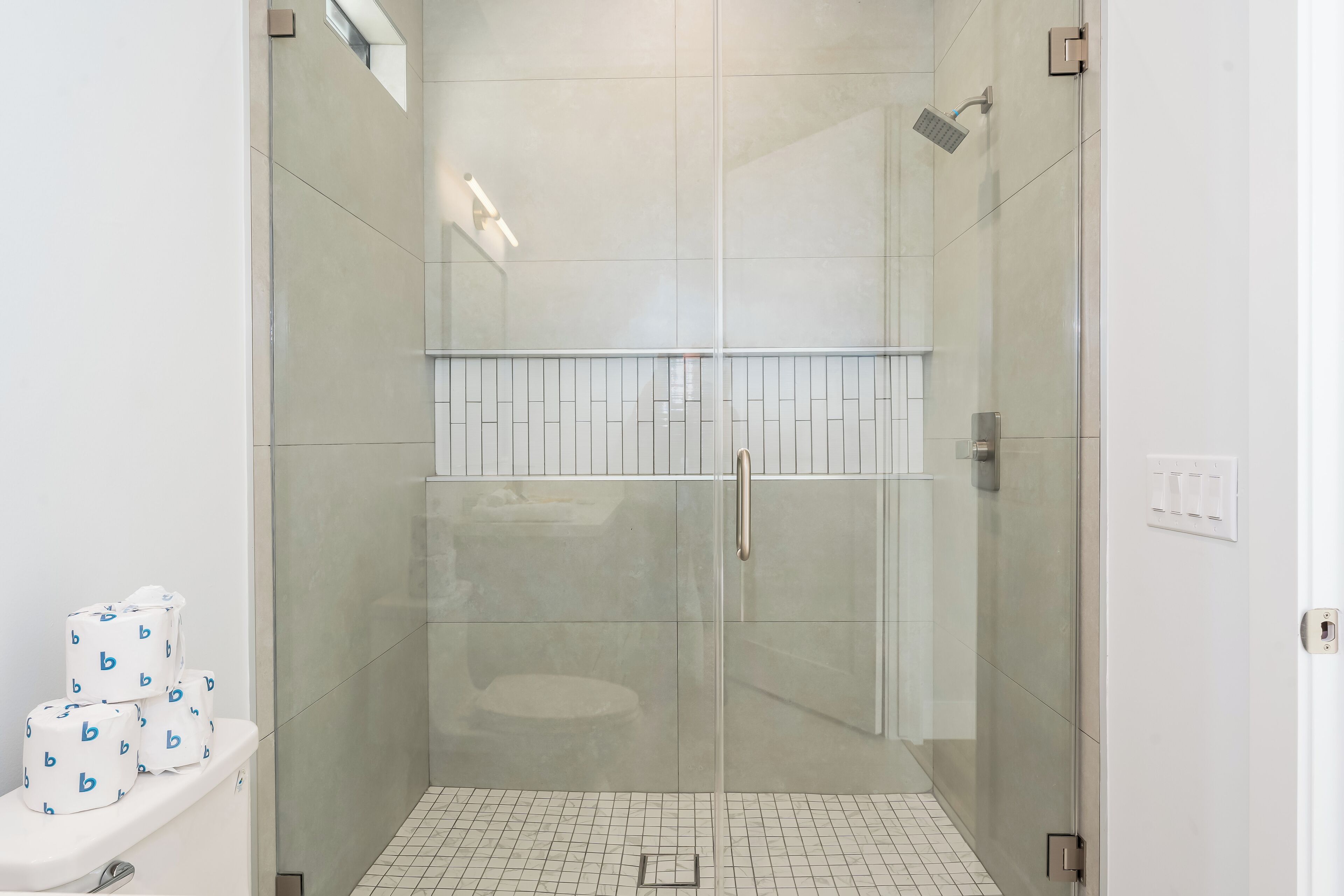 A modern bathroom with a glass-enclosed shower, a toilet with toilet paper, and a tiled floor.