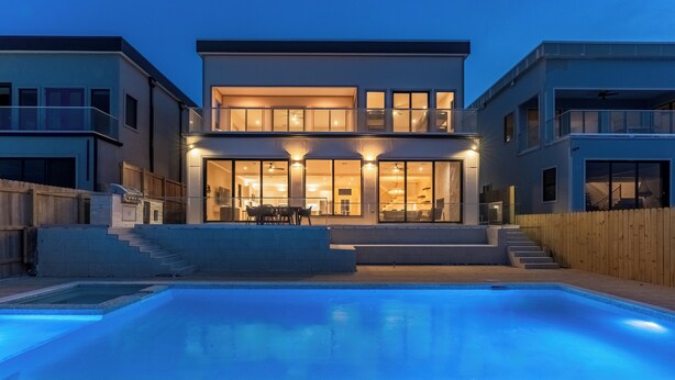 Uma casa moderna de dois andares com piscina, deck de madeira e interior bem iluminado.