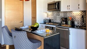 A modern kitchen with white cabinets, a microwave, a stove, and a sink. There is a dining area with a chair and a table, and two pendant lights above.