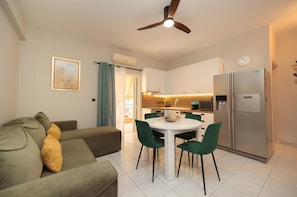 Un salon moderne comprenant un canapé, une table à manger avec des chaises, un ventilateur de plafond et un coin cuisine avec des placards et des appareils électroménagers.
