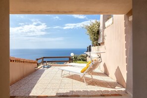 A balcony with a view of the sea, a tiled floor, and a lounge chair.