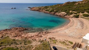A coastal landscape with a clear beach, rocky terrain, and sparse vegetation.
