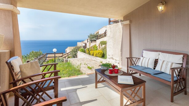A balcony with a wooden bench, chairs, and a table with a book and red mugs.