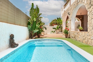 Une piscine dont le bord est recouvert de carreaux, entourée d’un mur de pierre, de plantes en pot et d’une statue de Bouddha.