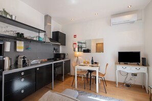 Une cuisine compacte dotée d’appareils électroménagers modernes, un coin repas avec une table et des chaises, un téléviseur posé sur un bureau et un miroir accroché au mur.
