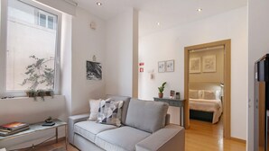 A modern living room with a sofa, a small table, a window with a plant, and a door leading to a bedroom. - Holiday Home 'Viola' with Wi-Fi and Air Conditioning (Faro)