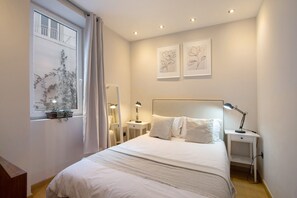 Une chambre à coucher comprenant un lit, des tables de chevet, une fenêtre avec des rideaux et des œuvres d’art accrochées au mur.