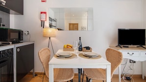 A compact kitchen with a microwave, stove, and a small refrigerator. There is a dining table with two chairs, a lamp, and a television on a desk. - Holiday Home 'Viola' with Wi-Fi and Air Conditioning (Faro)