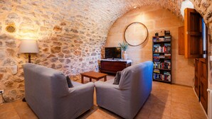 A stone-walled room with a fireplace, a television, a bookshelf, and two armchairs. - Villa 'Es Rafal De Baix' with Sea View, Wi-Fi and Air Conditioning (Son Servera)