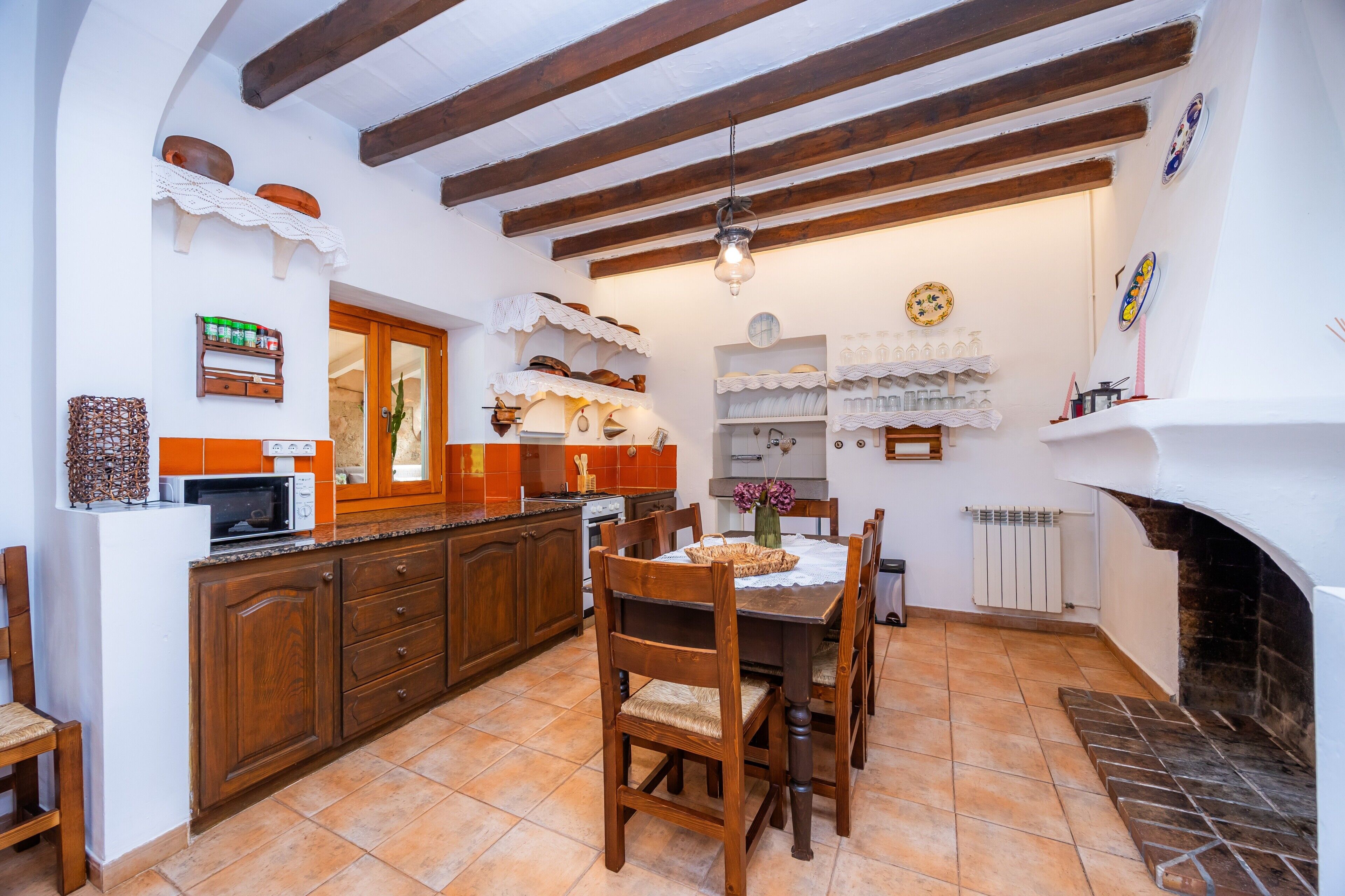 A kitchen with wooden cabinets, a dining table with chairs, a hanging light fixture, and a fireplace.