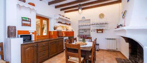 A kitchen with wooden cabinets, a dining table with chairs, a hanging light fixture, and a fireplace.