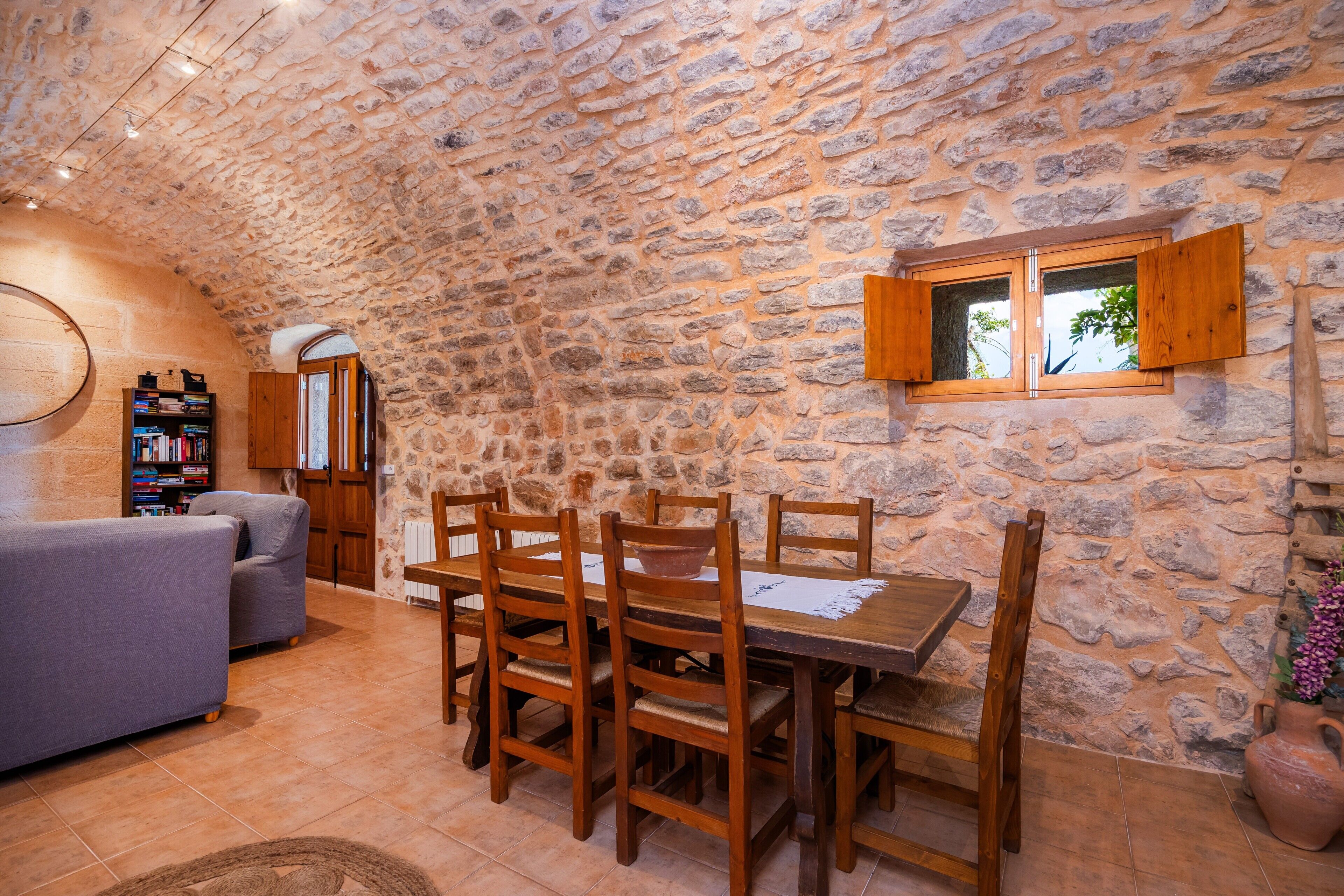 A stone-walled room with a dining table, chairs, a sofa, and a bookshelf.