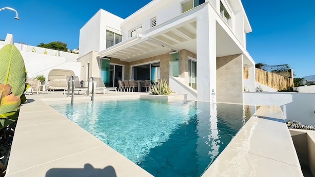 Una casa moderna con piscina, mobiliario exterior y un porche cubierto.