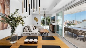 Una sala de estar moderna con comedor, un ventanal con vista a la ciudad y una planta en un jarrón.