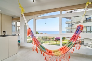 Een hangmat in een kamer met uitzicht op zee, een keukenhoek en een balkon.