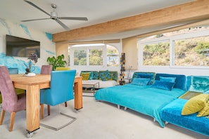 Een kamer met een bed, een bureau, een stoel, een plafondventilator en grote ramen.