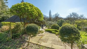 A stone pathway leading to a building with a sloped roof, surrounded by well-maintained hedges and trees. - Maison Le Clos Longlais - Welkeys (Grangues)