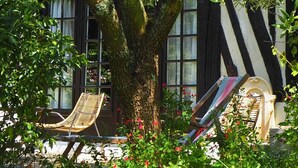 A tree with a bench under it, a striped wall, and a window with flowers. - Maison Le Clos Longlais - Welkeys (Grangues)