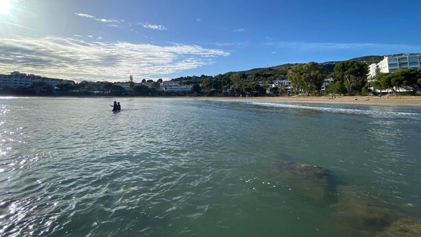 A coastal scene with a clear sky, calm water, and buildings along the shore.