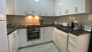 A modern kitchen with white cabinets, a stove, oven, dishwasher, and a coffee maker.
