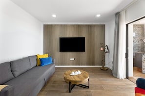 Una sala de estar moderna con un sofá gris, una mesa de centro redonda de madera, un televisor de pantalla plana montado en una pared a rayas y una chimenea de piedra.