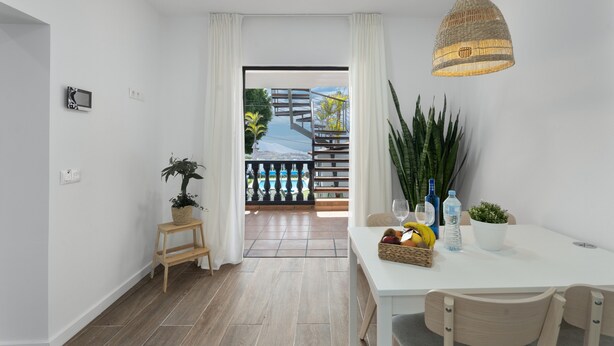 Een moderne eethoek met een witte tafel, stoelen, een hanglamp en een uitzicht door een glazen deur op een balkon.