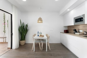 Una cocina moderna con una mesa de comedor, sillas, una lámpara colgante, una planta en maceta y un microondas.