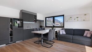Una cocina moderna con zona de comedor, un sofá gris y un amplio ventanal con vistas a la montaña.
