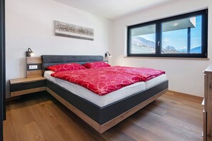 Une chambre moderne avec un lit, des tables de chevet, une fenêtre donnant sur les montagnes et une œuvre d’art accrochée au mur.