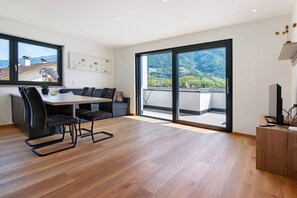 Un salon moderne comprenant un coin repas, de grandes portes-fenêtres coulissantes donnant sur un balcon et une vue sur un paysage montagneux.