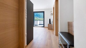 Un pasillo con suelo de madera, un banco, un televisor y vistas a un paisaje montañoso a través de un ventanal grande.
