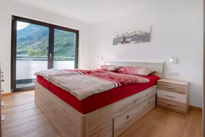 Une chambre dotée d’un grand lit, d’une table de chevet, d’une commode et offrant une vue sur un paysage montagneux grâce à une porte coulissante.