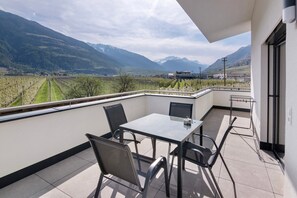 Uma varanda com mesa e cadeiras, vista para um vinhedo e montanhas ao fundo.