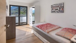 Una camera da letto moderna con un letto, una cassettiera, un quadro e vista su un paesaggio montuoso attraverso un'ampia finestra.