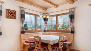 Ein Essbereich in Ecklage mit Holztisch und -stühlen, einer Bank und Blick auf einen Wald durch große Fenster.