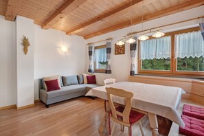 Una habitación acogedora con techo de madera, un sofá, una mesa de comedor y ventanas grandes con cortinas.